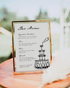 a menu on a wooden table next to a white and gold plate with some feathers