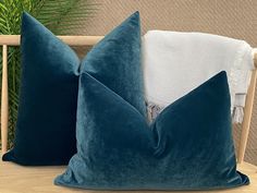 two blue pillows sitting on top of a wooden table next to a white towel and potted plant