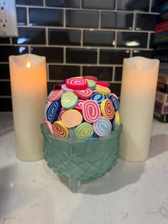 two candles sitting next to each other on top of a white counter with colorful candies in it