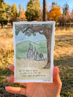 a person holding up a card with an image of two people under a tree in the background