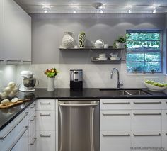 a kitchen with white cabinets and black counter tops, stainless steel dishwasher in the center