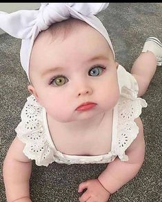 a baby wearing a white dress with a bow on it's head sitting on the floor