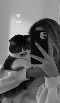 a woman is taking a selfie with her phone while holding a cat on her lap