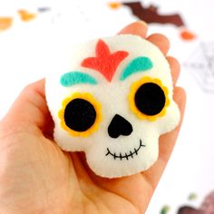 a hand holding a small white skull with yellow eyes and a red flower in it's hair