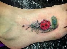 a ladybug tattoo on the foot of a person with a feather and flower