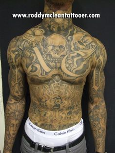 a man with many tattoos on his chest and arms is standing in front of a wall