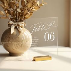 a table number sitting next to a vase with flowers in it and a gold bar