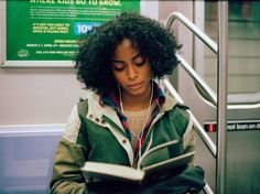 a woman sitting on a train reading a book and listening to headphones with earbuds in her ears