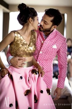 a man in a pink suit and woman in a gold top kissing on the cheek