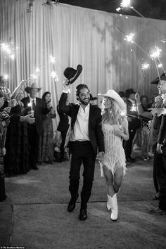 a man and woman walking through a crowd holding sparklers