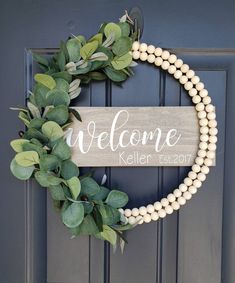 a welcome sign hanging on the front door with greenery and pearls around it's edges