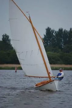 a man riding on the back of a sailboat in water with trees in the background