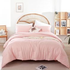 a bed with pink comforter and pillows in a room next to a plant on the floor