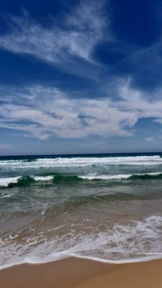 an ocean view with waves crashing on the shore and blue sky above it, as seen from the beach