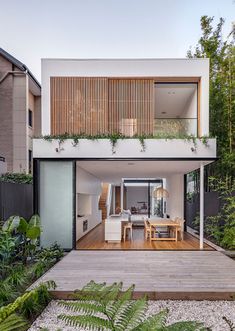 an outdoor living area with wooden decking and plants on the side of the house