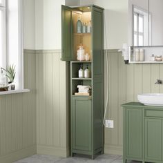 a bathroom with green cabinets and white sink in it's corner, next to a window