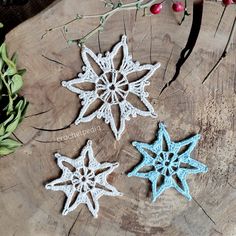 three crocheted snowflakes sitting on top of a tree stump next to berries