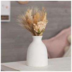 a white vase filled with dried flowers on top of a table