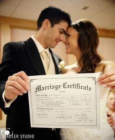 a bride and groom holding up a marriage certificate