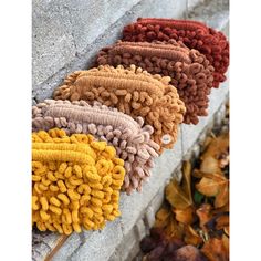 four different colored knitted items sitting on the side of a brick wall next to leaves