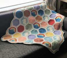 a crocheted blanket sitting on top of a couch in front of a window