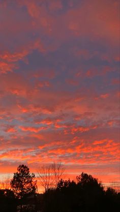 the sky is red and orange as the sun sets over some trees in the distance