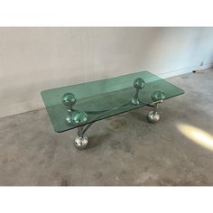 a glass coffee table with metal legs and balls on top, sitting in an empty room