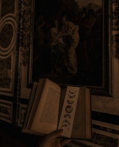 a person is holding an open book in front of a painting