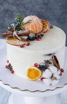 a white cake with oranges, berries and cinnamon on top sitting on a plate