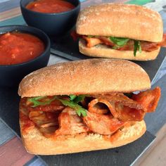 two sandwiches with meat, tomato sauce and lettuce sit on a black plate