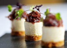 three small desserts are sitting on a black plate, with garnishes