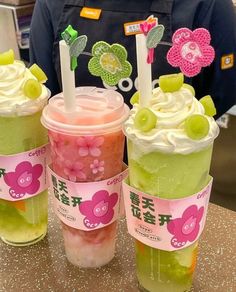 three cups filled with green and pink drinks on top of a table next to each other