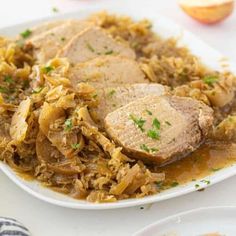 a white plate topped with meat covered in gravy next to an apple slice