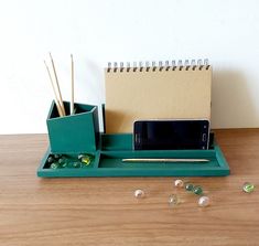 a desk with a cell phone, pen and pencil holder on it next to beads