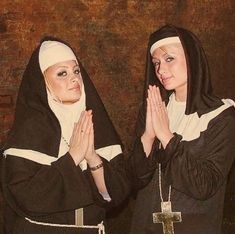 two women dressed in nun costumes standing next to each other with their hands clasped together