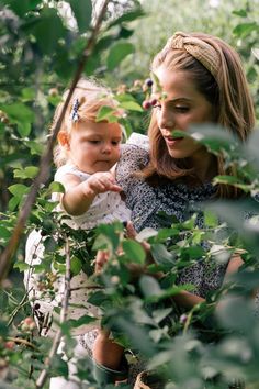 a woman holding a baby in her arms while picking berries from a tree with green leaves