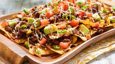 nachos with chili, cheese and avocado on a wooden platter