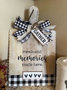 a wooden sign that says gather meals and memories made here with buffalo plaid ribbon on it