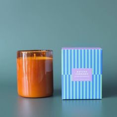 an orange candle next to a blue box on a grey surface with a green background