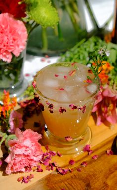 a glass filled with ice sitting on top of a wooden table next to pink flowers