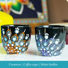 two coffee cups sitting next to each other on top of a white table with blue and orange designs