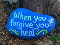 a blue rock with the words when you forgive you heal written on it, sits next to a tree