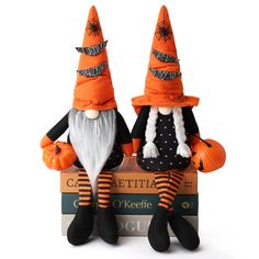 two halloween gnomes sitting on top of books with their heads turned to look like they are holding pumpkins