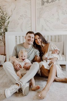 a man, woman and baby are sitting on the floor in front of a crib