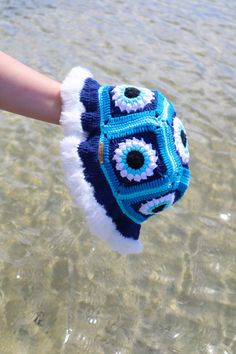 a hand holding a blue and white crocheted mitt in the clear water