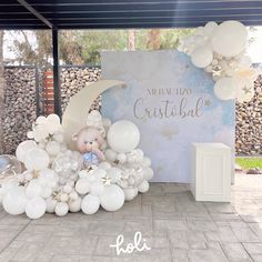 a teddy bear sitting on top of a pile of balloons in front of a sign