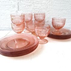 there are many pink glass cups and saucers on the white tablecloth with a brick wall in the background