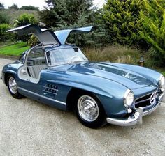 an old blue mercedes sports car with its hood open on the road in front of some trees