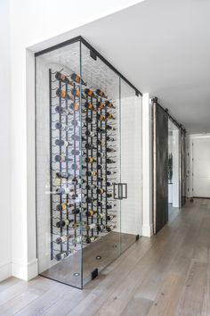 a glass wine rack in the middle of a room with wooden floors and white walls