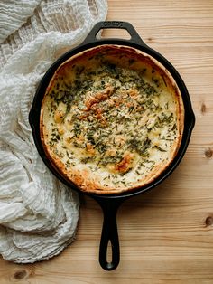 a skillet filled with cheese and spinach on top of a wooden table next to a white cloth